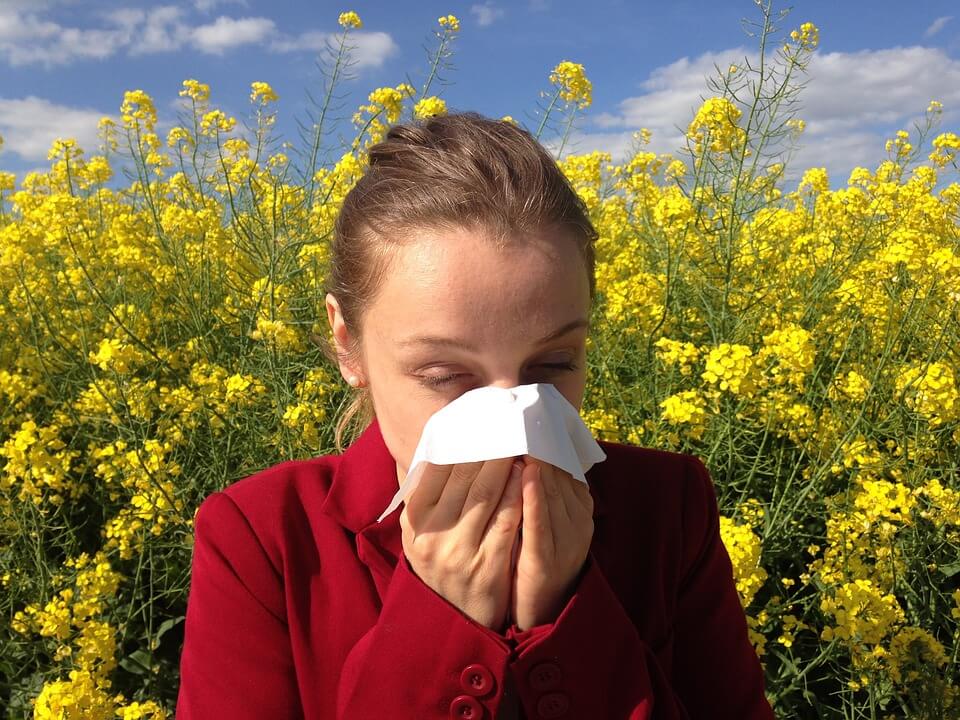 Ženska osoba puše nos zbog alergija, u pozadini su žuti cvjetovi 