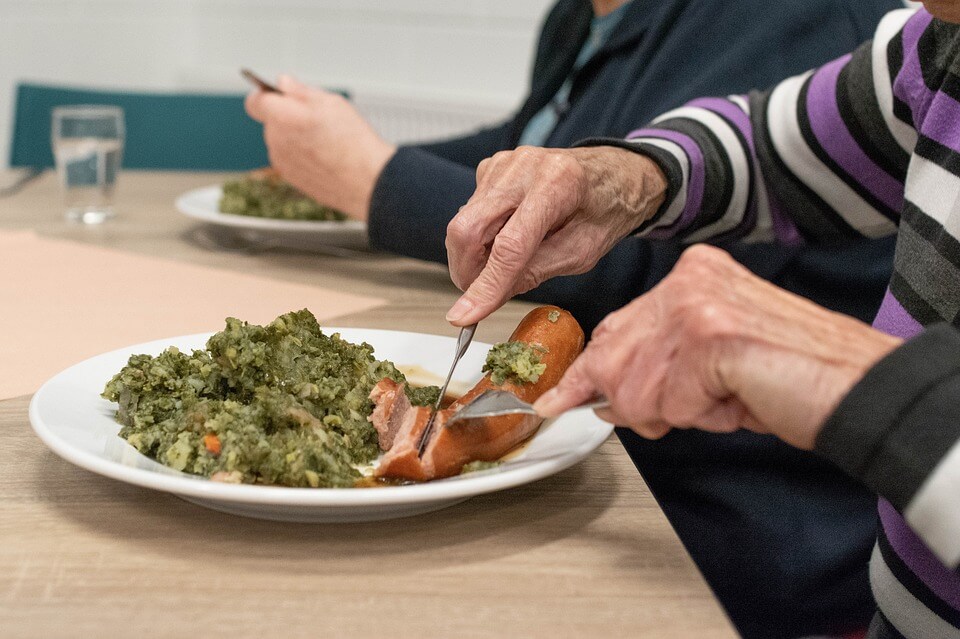 dvije starije osobe jedu hranu s tanjura