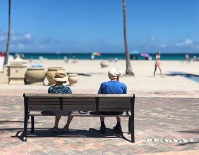 Starija žena i stariji muškarac sjede na klupi na plaži po suncu