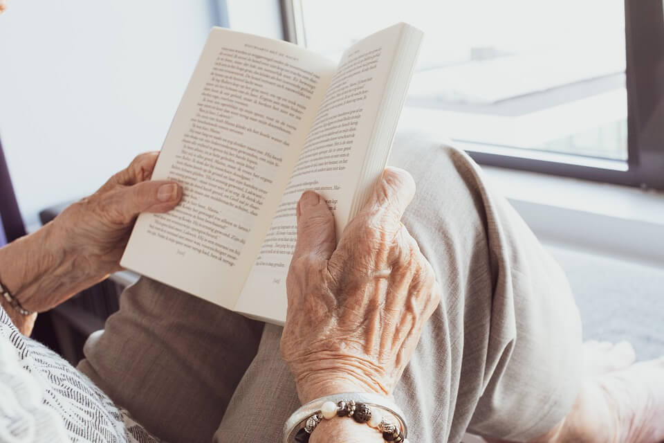 umirovljenica drži knjigu na koljenima i čita