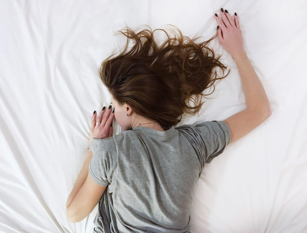 Žena smeđe kose leži na krevetu dok joj je desna ruka ispružena prema gore