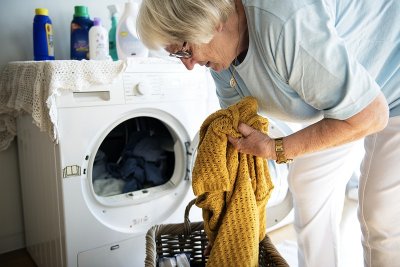 Umirovljenica stavlja u perilicu za pranje rublja žutu majicu