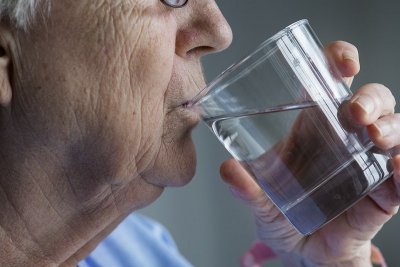 Stariji muškarac pije vodu iz čaše, pri čemu su u prvom planu čaša i njegovo lice