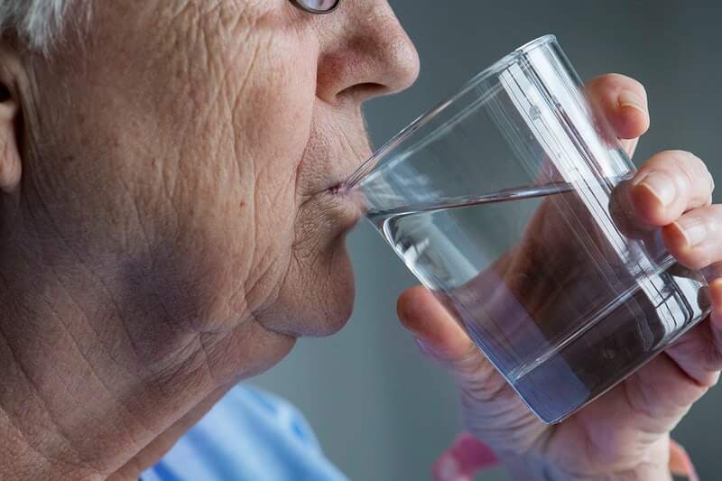 Stariji muškarac pije vodu iz čaše, pri čemu su u prvom planu čaša i njegovo lice