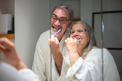 Stariji bračni par pere zube ispred ogledala