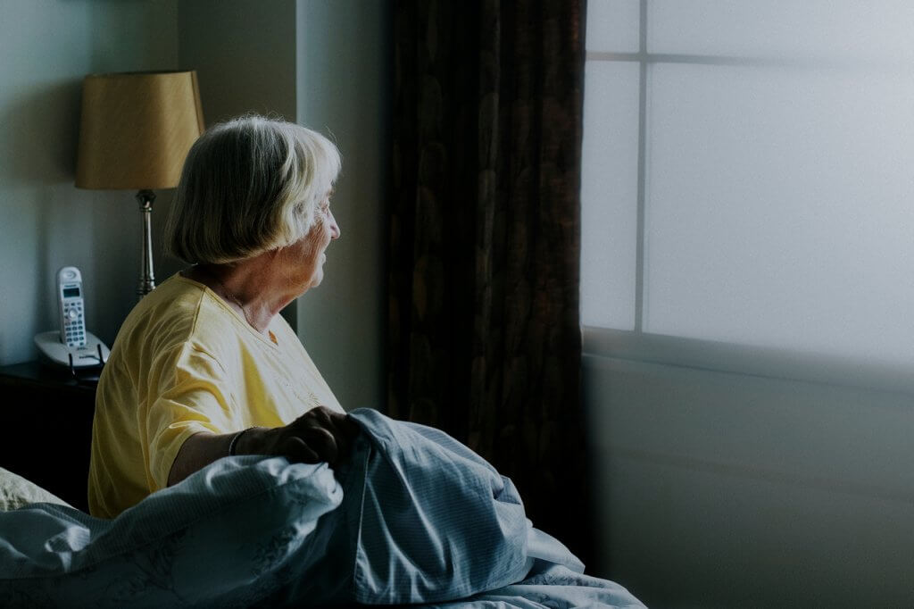 Starija ženska osoba sjedi u krevetu i gleda prema prozoru