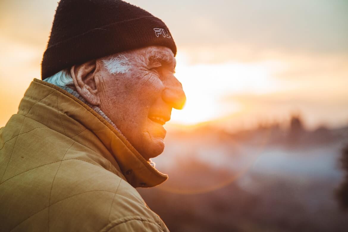 umirovljenik s kapom na glavi gleda u daljinu, dok je u pozadini zalazak sunca