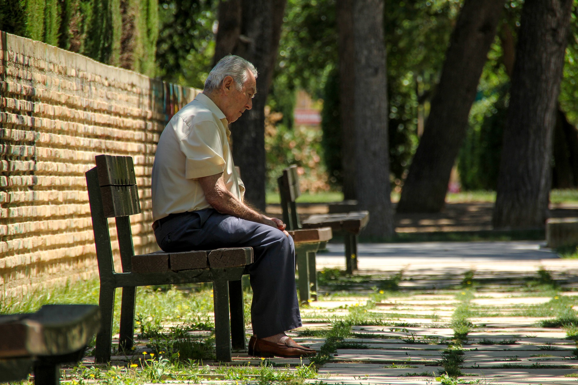 Stariji umirovljenik sjedi na klupi u parku