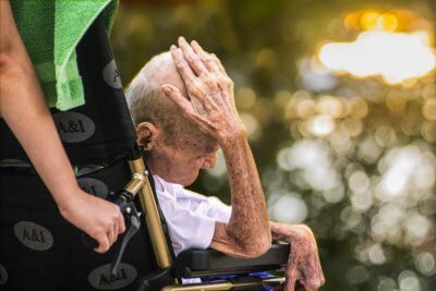 Stariji umirovljenik se drži za glavu u kolicima koja gura druga osoba