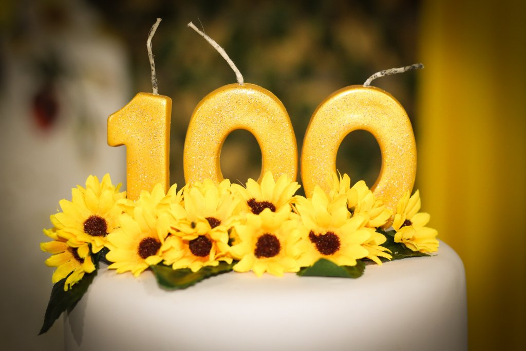 torta ukrašena suncokretima i svjećicama s brojem 100