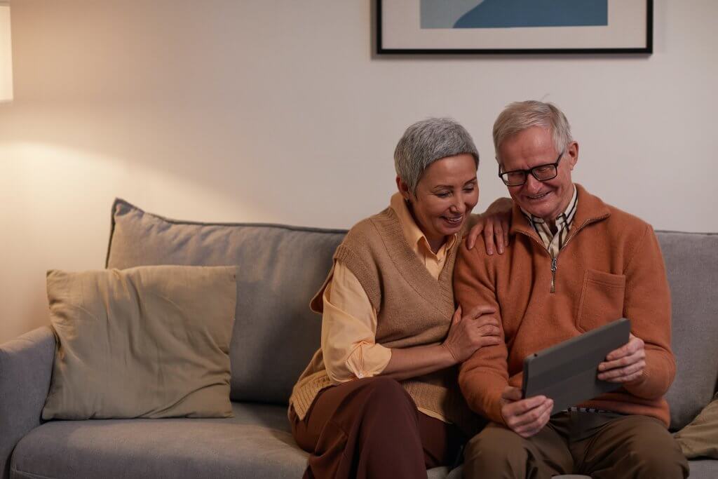 Stariji bračni par sjedi na trosjedu u dnevnoj sobi i gleda u tablet