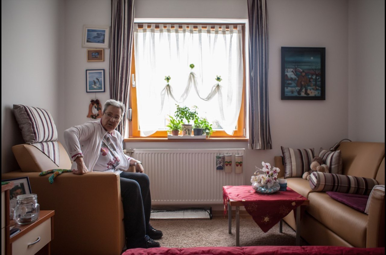 Umirovljenica u stanu u sklopu stambene zajednice sjedi i gleda prema fotoaparatu
