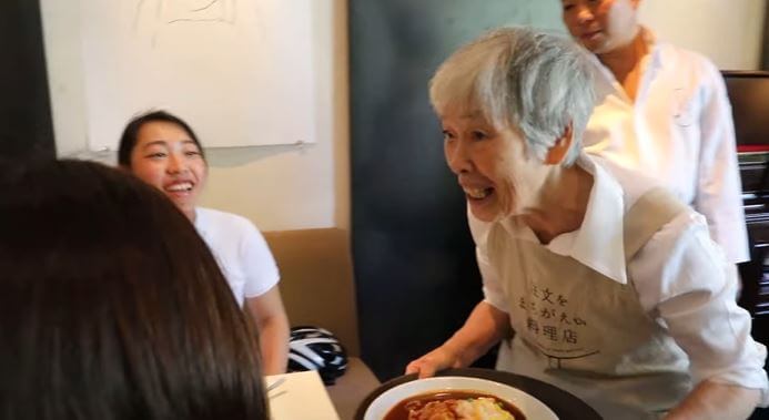 Starija ženska osoba donosi hranu u restoranu u kojem rade samo konobari koji imaju demenciju