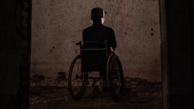 Osoba s invaliditetom u invalidskim kolicima sjedi u tami okrenuta prema zidu