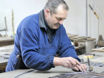 Umirovljenik u radnoj odjeći obrađuje metal u radionici