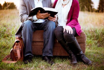 Žena i muškarac sjede na kauču nasred livade i čitaju knjigu.