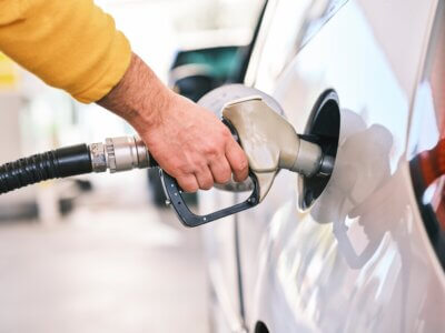 Muškarac u žutom džemperu toči gorivo u bijeli automobil na benzinskoj crpki.