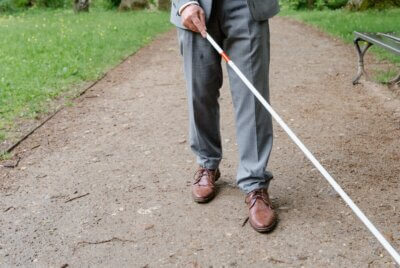 Stariji muškarac istovremeno drži kišobran i koristi štap za slijepe i slabovidne osobe
