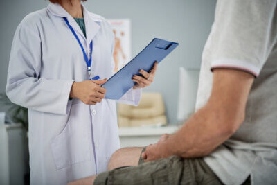 Liječnica u bijeloj kuti postavlja pacijentu pitanja u vezi njegovog zdravstvenog stanja.
