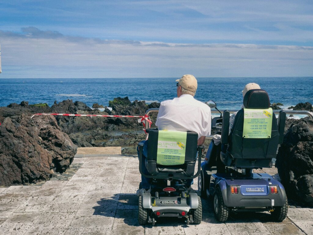 Par umirovljenika sjedi u kolicima na električni pogon i promatra obalu.