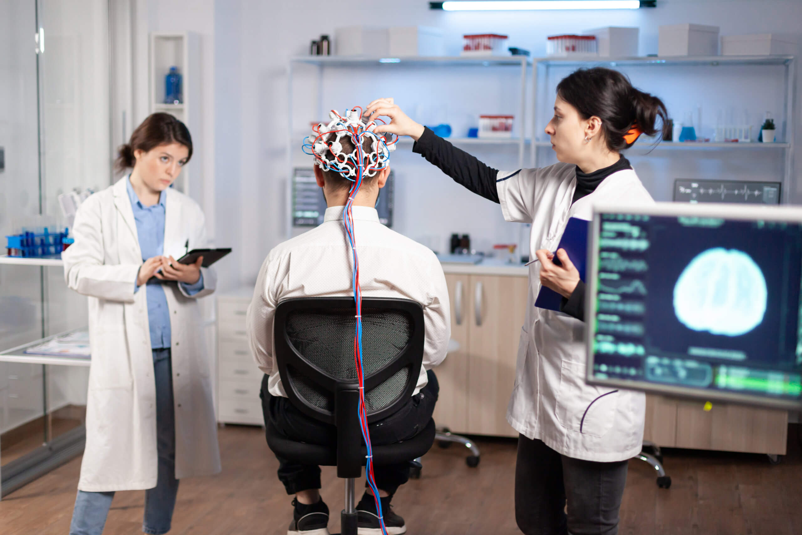 Pacijent na skeniranju moždanih valova koji sjedi u laboratoriju za neurološka istraživanja dok ga liječnice nadziru.