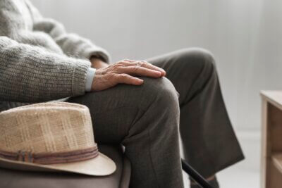 Umirovljenik u sivom puloveru i tamnosivim hlačama sjedi u stolici i drži dlanove na nogama.
