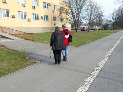 Mlađa osoba iz Crvenog križa vodi stariju osobu