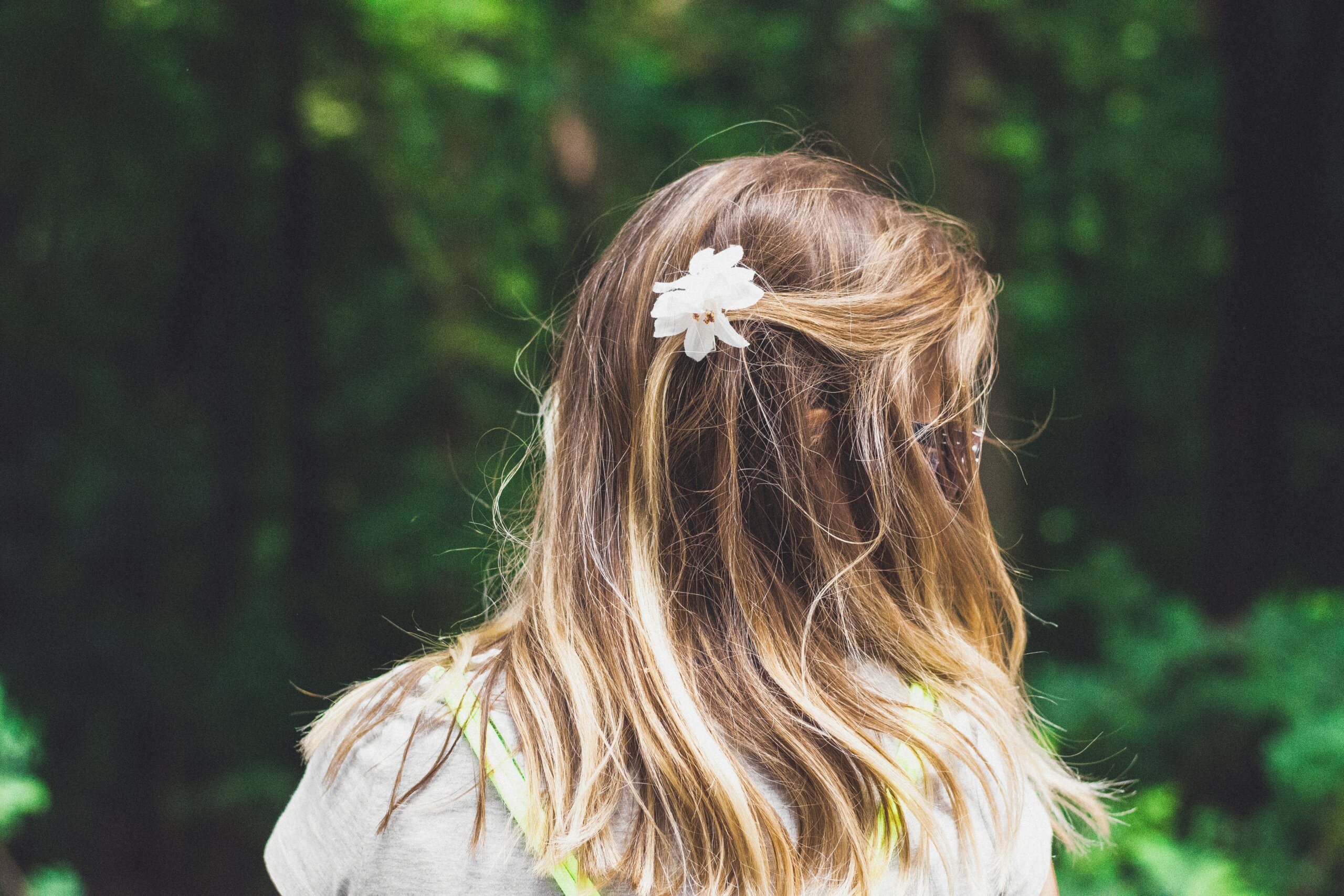 Bijeli cvijet u plavoj kosi djevojčice u prirodi.