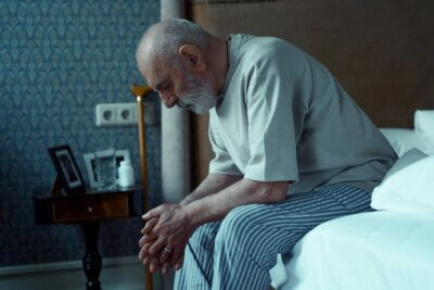 Umirovljenik sjedi na krevetu u pidžami i gleda u pod.