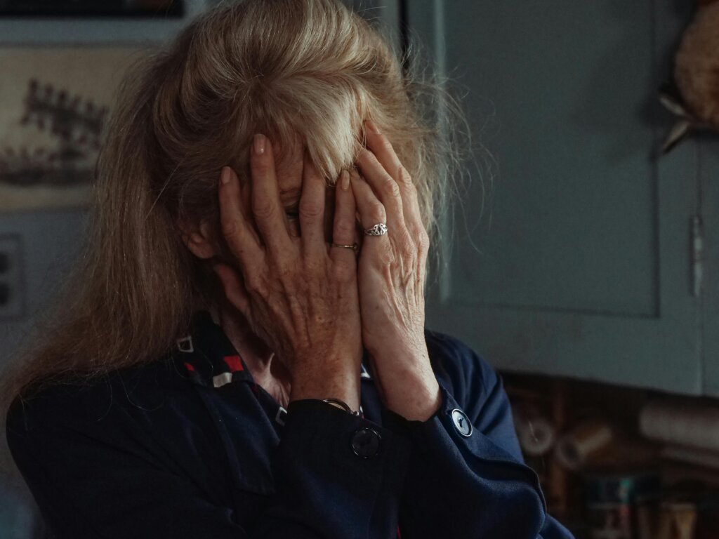 starija žena rukama pokriva lice