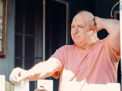 Proćelavi uznemireni umirovljenik u svijetloj majici drži se jednom rukom za glavu