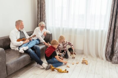 djed sjedi na kauču i svira ukulele, baka sjedi pored njega, dvoje unuka se igra na podu s igračkama