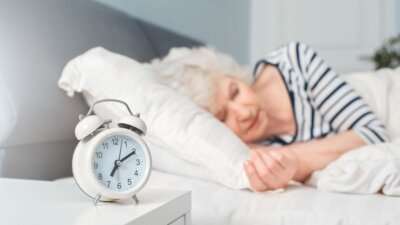 Umirovljnica spava u krevetu pored budilice