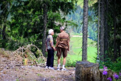 Umirovljenica i umirovljenik se drže za ruke u šumi pored borova