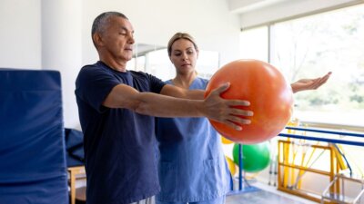 Stariji muškarac na fizioterapiji drži narančastu loptu u ruci
